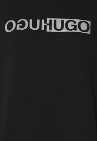 Tissu noir avec le mot "HUGO" imprimé en grandes lettres blanches, en gras, miroir et répété deux fois sur toute la surface.