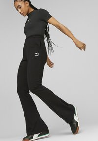 Svart ribbad träningsöverdel parat med svarta utsvängda byxor med en logo. Svarta och vita sneakers med turkos accent. Släta texturer.