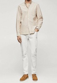 Camisa de botones a rayas beige y blanca con un bolsillo en el pecho, combinada con pantalones blancos y zapatos de ante marrón, con un ajuste casual.