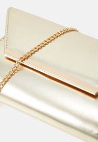 Zlatna clutch od umjetne kože s zlatnim lančićem i metalnim akcentom. Ima glatku površinu i presavijen dizajn.