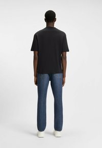 Black short-sleeve t-shirt viewed from the back, paired with blue straight-leg jeans and white sneakers. Smooth fabric, minimal design.