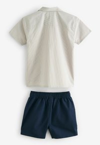 Hemd mit kurzen Ärmeln in hellbeige mit dezenten Streifen, kombiniert mit dunkelblauen Shorts mit elastischem Bund, glatte Textur und klassischer Schnitt.