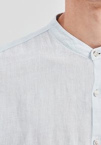 Jasnoniebieska lniana koszula z kołnierzykiem stójką, o fakturowanym wykończeniu i naturalnych guzikach na przedniej plisie.