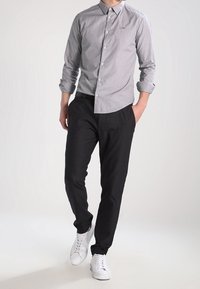 Męska koszula z długim rękawem, szara w paski, zestawiona z czarnymi dopasowanymi spodniami i białymi sneakersami. Slim fit, klasyczny krój kołnierza.