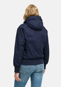Jacket con cappuccio di un blu navy, con chiusura a zip, polsini e orlo a coste, e tasche laterali, caratterizzato da una texture di tessuto liscia e da un design minimalista.