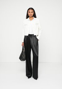 Λευκό σακάκι από τουίδη με μεταλλικά κουμπιά, συνδυασμένο με ψηλόμεσες, μαύρες σατέν παντελόνες σε φαρδιά γραμμή. Μαύρη τσάντα χειρός με χρυσές λεπτομέρειες.