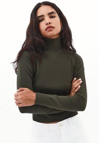 Olijfgroene, aansluitende coltrui van een zachte stof met geribbelde manchetten en zoom. Draagt in combinatie met hooggerokte witte broek.