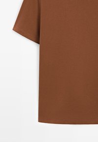 T-shirt marron à manches courtes en tissu doux, avec un col rond et un ourlet droit, présentant une texture lisse et un design minimaliste.