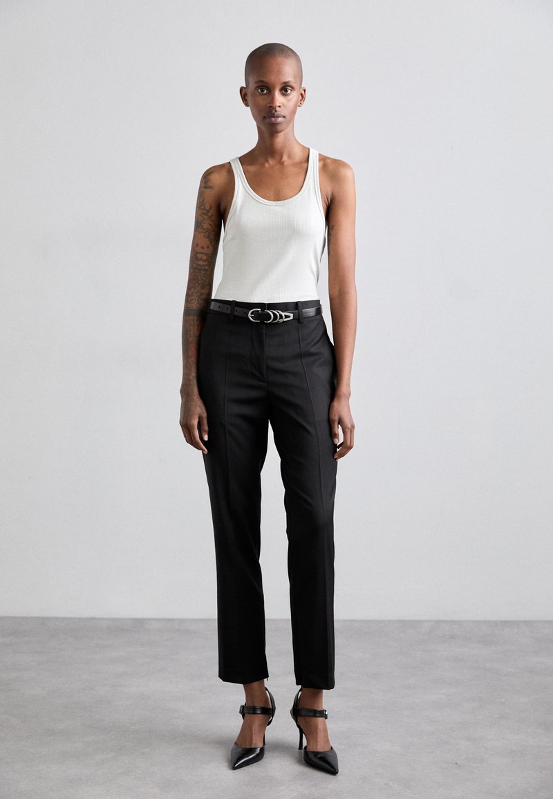 Black tailored trousers with a slim fit, paired with a white ribbed tank top. The outfit includes black pointed heels and a black belt with a silver buckle.