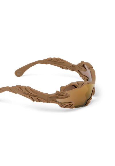 Lunettes de soleil marron avec monture sculptée en forme de feuille texturée et verres miroirs ambrés reposant sur un fond blanc.