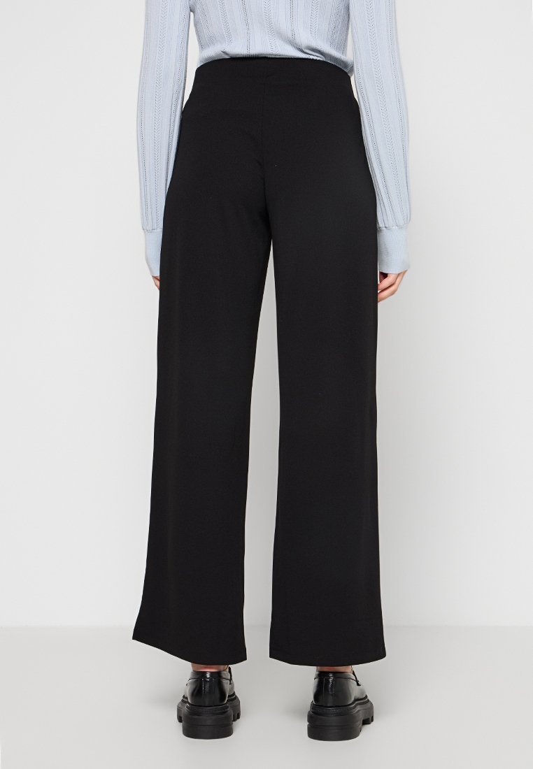 Pantaloni neri a vita alta a gamba larga con una texture liscia e un design minimalista, abbinati a scarpe nere.