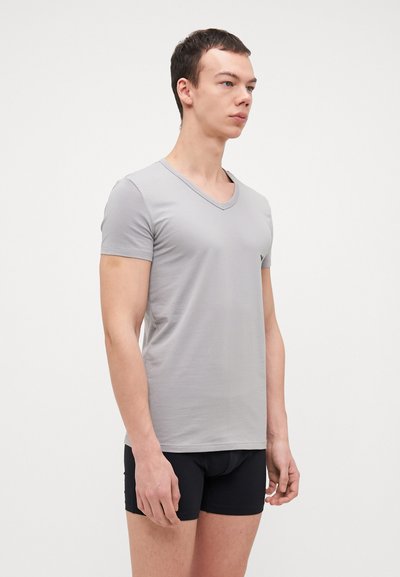 Graues V-Ausschnitt-T-Shirt aus weichem Stoff; kurze Ärmel, taillierte Form, schlichtes Design ohne Muster oder Akzente, getragen mit schwarzen Shorts.