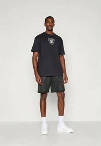 Μαύρο κοντομάνικο μπλουζάκι με κεντρικό λογότυπο και αντίστοιχα μαύρα κοντά παντελόνια από δίχτυ. Λευκά αθλητικά παπούτσια ολοκληρώνουν το αθλητικό σύνολο.