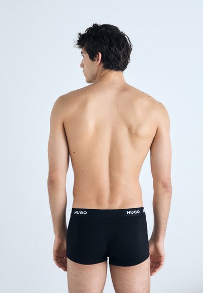 Boxer-briefs noirs à coupe ajustée avec un logo HUGO en caoutchouc sur la ceinture. Tissu lisse avec un design uni, vu de dos.