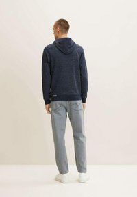 Sudadera con capucha navy de tejido texturizado, combinada con jeans gris claro y zapatillas blancas. La sudadera presenta un dobladillo y puños acanalados.