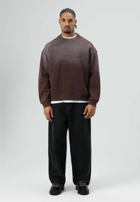 Bruine sweatshirt met verloopkleur en verhoogde stippen, gecombineerd met losse zwarte broek en zwarte schoenen met roze veters. Eenvoudig wit T-shirt eronder.