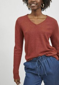 Pull en V rouge en maille douce avec des poignets côtelés, associé à un pantalon bleu à cordon de serrage. Design simple et coupe décontractée.