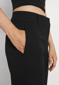 Pantalon noir ajusté avec une texture de tissu lisse, doté de poches latérales et d'une taille épurée, vu près de la taille.