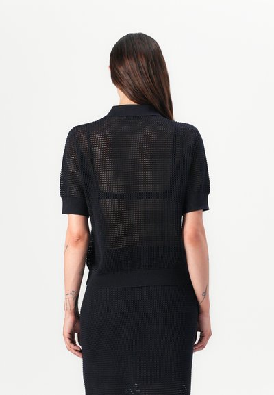 Polo scurt din tricot negru cu un țesut texturat și deschis. Prezintă un guler clasic și un tiv cu nervuri, lăsând să se vadă pielea prin țesătură.
