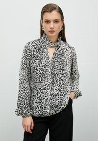Blus med leopardmönster i svart och vitt, med knytkrage, långa ärmar, knäppning fram och samlade manschetter, tillverkad av lättviktigt material.