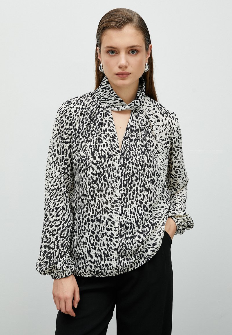 Blus med leopardmönster i svart och vitt, med knytkrage, långa ärmar, knäppning fram och samlade manschetter, tillverkad av lättviktigt material.