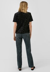 Zwarte pailletten top met korte mouwen en een ontspannen pasvorm, gecombineerd met hooggeknoopte, vervaagde grijze jeans en zwarte sandalen.