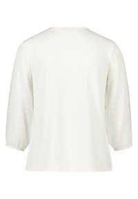 Blouse blanche à manches longues avec un col rond et des poignets élastiques. Tissu doux et lisse avec une coupe ample et sans motifs ou designs visibles.