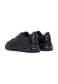 Un par de zapatillas de cuero negro con suelas gruesas que cuentan con unidades de amortiguación de aire visibles sobre un fondo blanco.