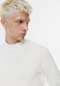 Weißer Pullover mit Stehkragen, geripptem Kragen, figurbetonter Silhouette und glatter Textur. Verfügt über dezente Nahtdetails an den Schultern.