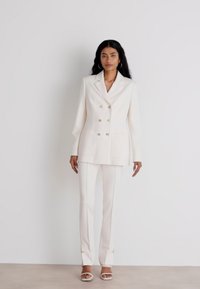 White tailored double-breasted blazer with metallic buttons and pockets, paired with matching slim-fit pants featuring side piping and button accents.