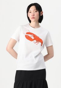 T-shirt de algodão branco com um grande gráfico de lagosta vermelha. Manga curta e decote redondo, combinado com uma saia preta. Textura suave.
