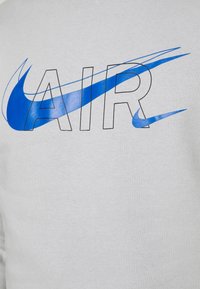 Grå tröja med djärv svart text "AIR" och en blå Nike swoosh-grafik. Tillverkad av bomull med en slät textur och avslappnad passform.