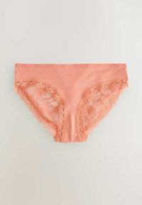 Perzikkleurige panties met kantafwerking, gemaakt van een gladde stof, met delicate, golvende randen en een naadloos ontwerp aan de zijkanten.