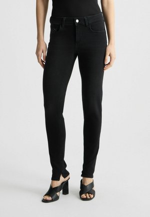 Jeans skinny en denim noir avec une taille mi-haute, des poches avant et une texture subtile. Associés à des talons ouverts noirs avec un design de talon bloc.