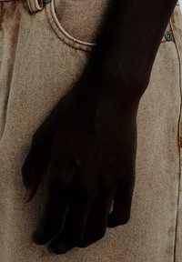 Μπεζ τζιν denim με ένα εμφανές χέρι που ακουμπά πάνω στο ύφασμα, παρουσιάζοντας την υφή και τις λεπτομέρειες των ραφών.