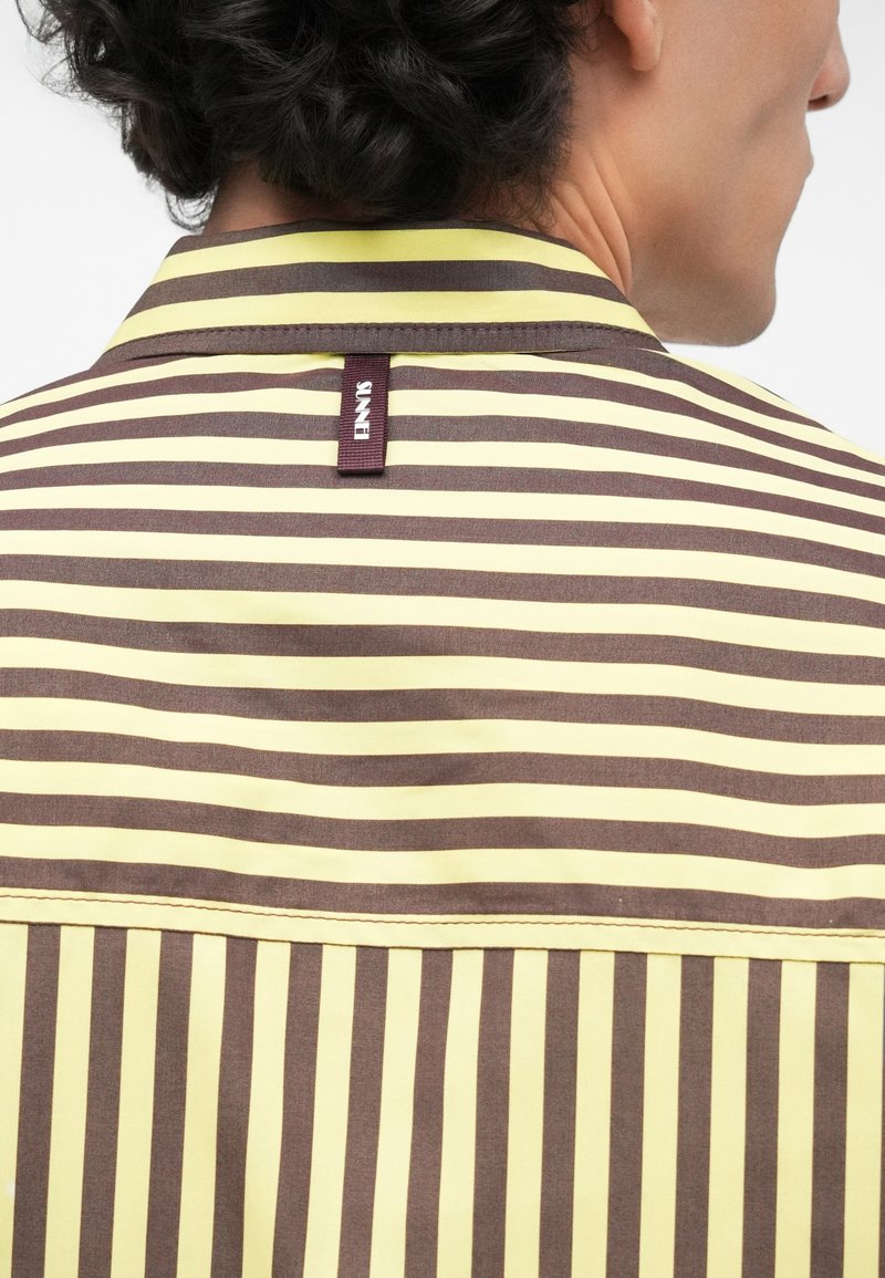 Striped shirt featuring alternating thick brown and light yellow lines. Designed with a collar and a label at the back neckline.