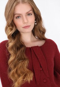 Bordeaux trui met een gestructureerde breisteek en een strikdetail bij de halslijn. Hij heeft grote knopen en een brede, ronde halslijn.