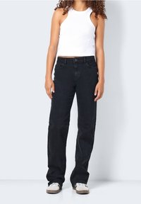 Svarta denimjeans med hög midja och rak passform. Kombinerat med en vit ribbad linne och beige sneakers. Slät textur, avslappnad stil.