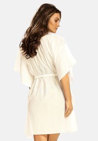 Biała, sięgająca do kolan sukienka z lekkiego materiału, z wcięciem w talii, szerokimi rękawami kimono i gładką fakturą.