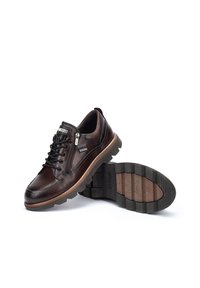 Zapatos de cuero marrón con punta redonda, parte frontal con cordones y cremallera lateral. Destacados por su suela de goma gruesa y acentos marrones contrastantes.