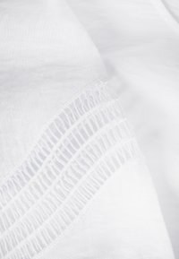 Tissu blanc présentant un motif texturé avec de fines lignes verticales et des accents légèrement surélevés le long du bord, offrant une profondeur visuelle.