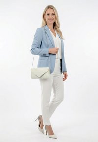 Frau trägt hellblauen Blazer, weiße Bluse, weiße Hose, beige Absätze und hält eine weiße Clutch mit silberner Kette.