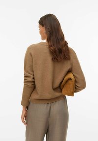 Brun stickad tröja med rund halsringning, avslappnad passform och ribbade muddar, kombinerad med ljusbruna byxor; håller en mjuk beige jacka.