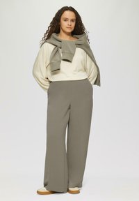 Hellbeige langärmliges Oberteil, grauer Pullover lässig um die Schultern drapiert, graue weite Hose und beige Sneakers mit braunen Sohlen. Neutrale Farbpalette.