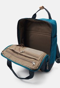 Batoh s tyrkysovým a námořnickým modrým vnějškem, hnědým vnitřkem. Obsahuje dva zipové oddíly, textilní držadla a strukturovanou kapsu.