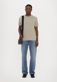 Beige kortermet t-skjorte, blå slengjeans, svarte sko og en liten svart skulderveske, med et enkelt design og nøytrale farger.