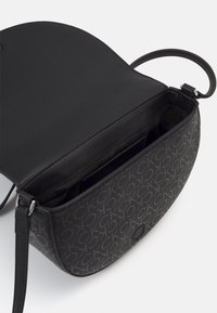 Borsa a tracolla nera realizzata in materiale testurizzato, caratterizzata da una forma curvata, tasche interne e un motivo con logo sulla parte frontale.