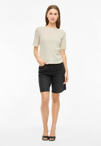 Top texturizado verde claro con mangas cortas, combinado con shorts de mezclilla negros. El conjunto presenta un ajuste relajado y un sutil patrón en olas.