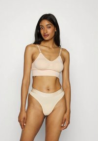 Beige bralette med justerbare stropper og sløyfedetalj; kombinert med matchende tanga med logo-bånd. Glatt, elastisk stoff.