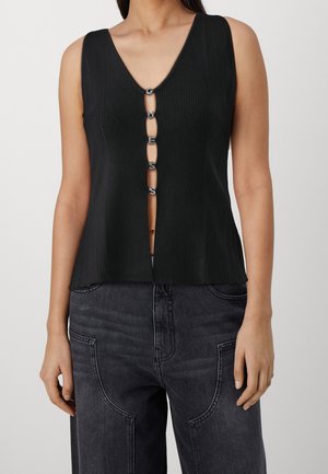 Mouwloze zwarte geribbelde top met vijf decoratieve zilveren gespjes aan de voorkant, gecombineerd met hooggetailleerde donkergrijze jeans met grote voorzakken.